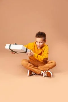 Boy sitting on the floor holds out a gift box Stock Photos