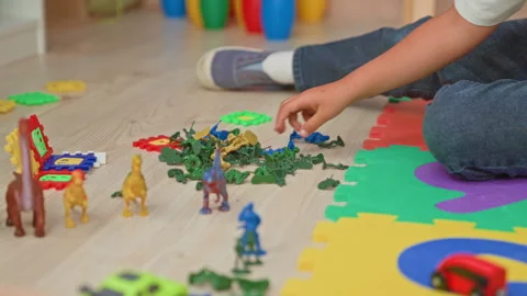 Boy sitting on a foam puzzle mat arranging toy dinosaurs, plastic soldiers .. Stock Footage 337373237