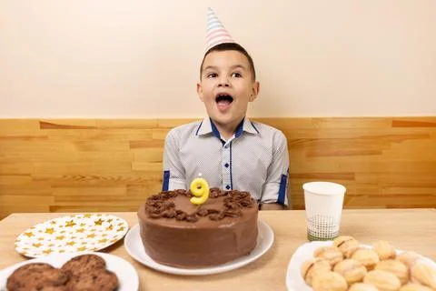 A boy is sitting in front of a table with a festive cake, in which a candle.. Stock Photos