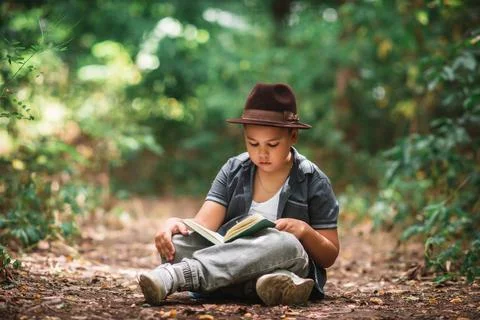 Boy sitting on the ground reading an open book Stock Photos