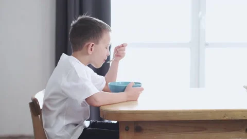 Boy sitting at home at the table and eating Stock Footage 169481892