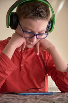 Boy sitting at home using his mobile phone with headphones Stock Photos