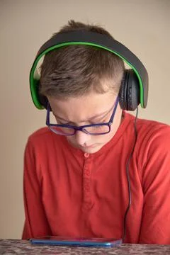 Boy sitting at home using his mobile phone with headphones Stock Photos