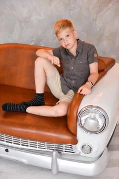 Boy sitting in the interior of the studio on a chair in the form of a retro car Stock Photos