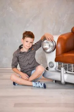 Boy sitting in the interior of the studio on a chair in the form of a retro car Stock Photos