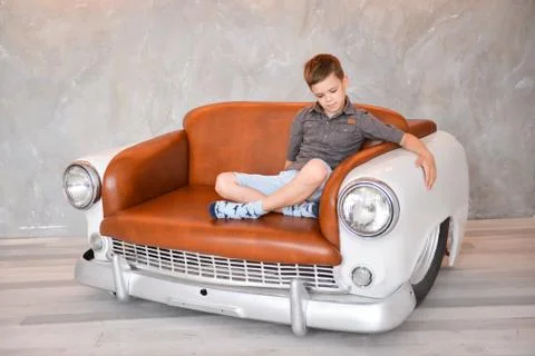 Boy sitting in the interior of the studio on a chair in the form of a retro car Stock Photos