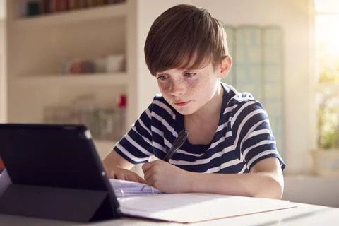 Boy Sitting At Kitchen Counter Doing Homework Using Digital Tablet 스톡 사진
