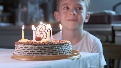 Boy sitting at kitchen table and blowing candles on birthday cake, making wish Stock Footage 119278145