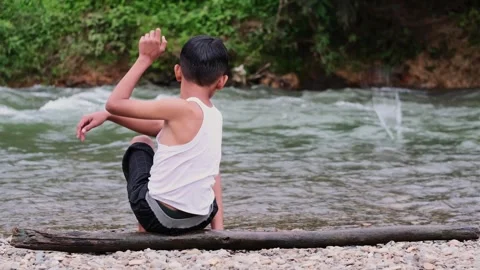 Boy is sitting on a log in the water 스톡 동영상 319750044