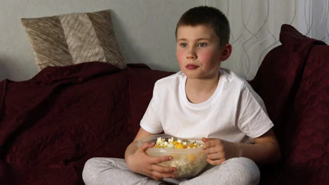 Boy sitting in lotus pose on sofa and he was scared by movie at home. Stock Footage 154404021