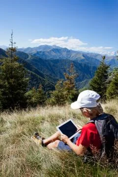 Boy sitting in a mountain meadow using a tablet computer Stock Photos