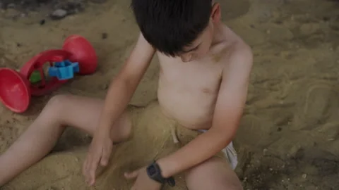 Boy sitting in only underpants on the sand in the garden of the house, covering Stock Footage 255526989
