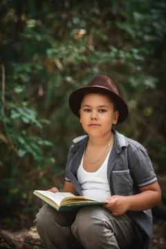 Boy sitting reading an open book in forest portrait Foto stock