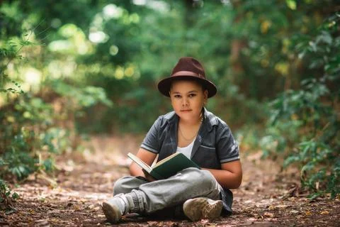 Boy sitting reading an open book looking at camera Foto stock