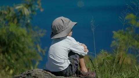 Boy sitting on a rock looing out to sea Stock Footage 84098003
