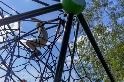 Boy sitting on rope web on playground against sky. Children's games in fres.. Stock Photos
