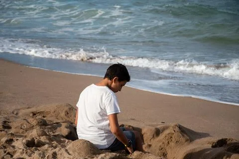 Boy sitting on the sand on the beach inside a sand hole Stock Photos