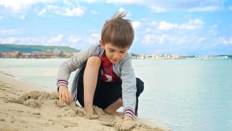 Boy sitting on the sea beach, digging and playing with sand. Concept of tou.. Stock Photos