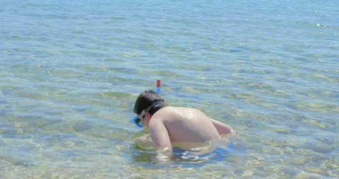 The boy is sitting in the shallows on the beach and playing. Stock Footage 133085677