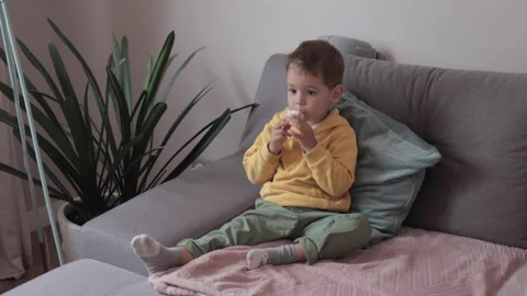 The Boy is sitting on the sofa and eating ice cream. 스톡 동영상 138644961
