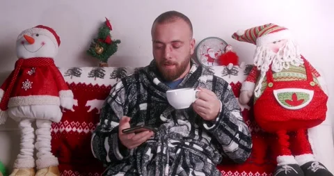Boy sitting on the sofa with tea while chatting on the phone at Christmas Stock Footage 144355588
