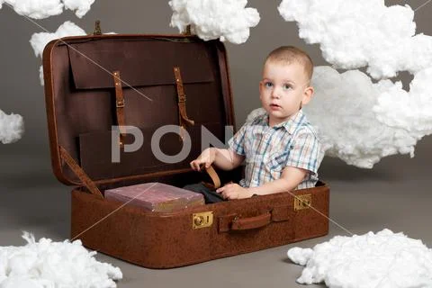 The boy is sitting in a suitcase and going on a journey, clouds of cotton woo Stock Photos