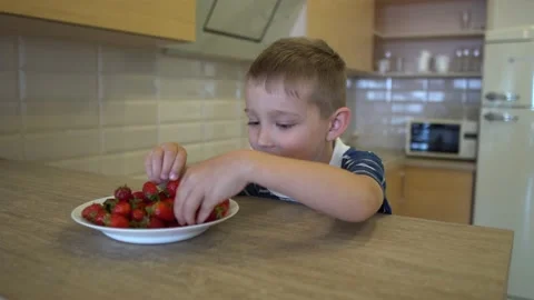 The boy is sitting at the table and eating strawberries Video stock 168074247