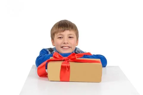 The boy is sitting at the table, in front of him is a gift in paper packaging Stock Photos