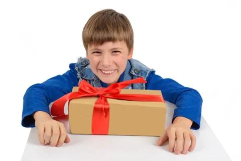 The boy is sitting at the table, in front of him is a gift in paper packaging Stock Photos