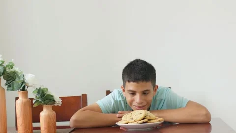 A boy is sitting at a table with a plate of cookies in front of him Stock Footage 310405805