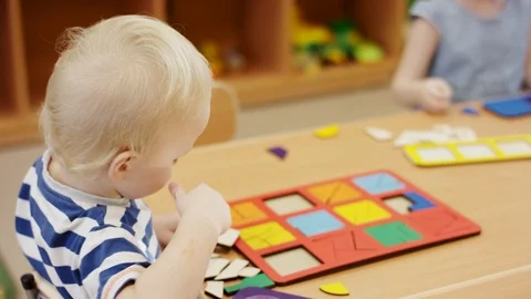 The boy is sitting at the table, trying to collect the puzzle from different Stock Footage 111076903