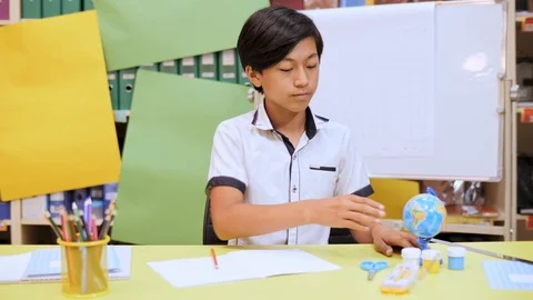 The boy is sitting at the table twisting the globe, after thinking, begins to Stock Footage 93498139
