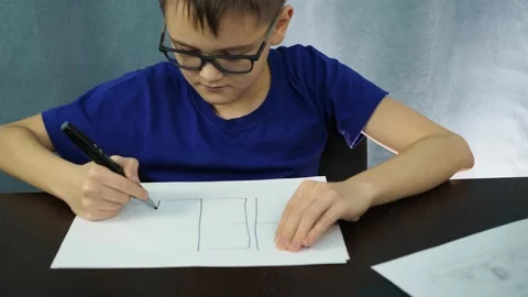The boy sitting at the table writes the word help on paper. Learning at home is Stock Footage 145317323