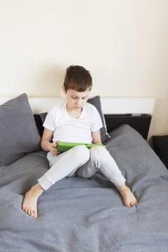 Boy sitting with a tablet on bed.Distance learning online education. Child wi Stock Photos
