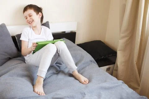 Boy sitting with a tablet on bed.Distance learning online education. Child wi Stock Photos