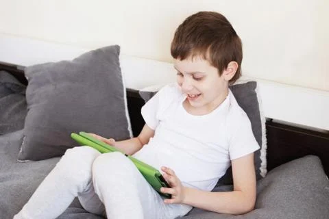 Boy sitting with a tablet on bed.Distance learning online education. Child wi Photos
