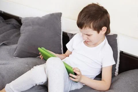 Boy sitting with a tablet on bed.Distance learning online education. Child wi Stock Photos