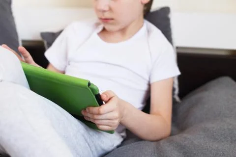 Boy sitting with a tablet on bed.Distance learning online education. Child wi 스톡 사진