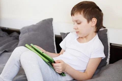 Boy sitting with a tablet on bed.Distance learning online education. Child wi Stock-Fotos
