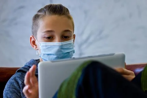 Boy sitting with tablet in mask during quarantine at home Stock Photos