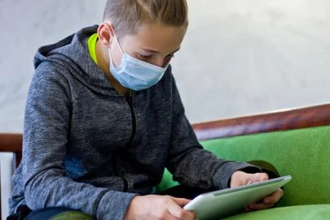Boy sitting with tablet in mask during quarantine at home Stock Photos