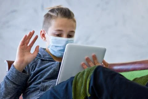 Boy sitting with tablet in mask during quarantine at home Stock Photos