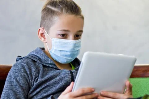 Boy sitting with tablet in mask during quarantine at home Stock Photos