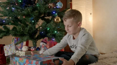 Boy sitting under the tree and unpacking Christmas gift Stock-Footage 67712490