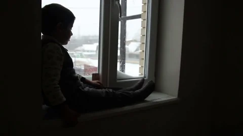 Boy sitting on a window sill 스톡 동영상 75811958