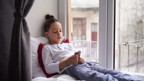 Boy sitting on the window sill uses a smartphone Stock Footage 91171674