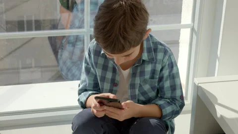 Boy sitting on windowsill, using mobile cell phone, watching video, playing game Stock Footage 171090501