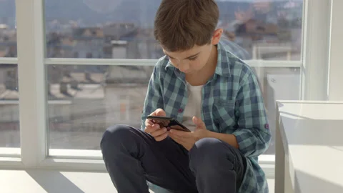 Boy sitting on windowsill, using mobile cell phone, watching video, playing game Stock Footage 171090541