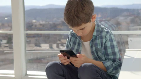 Boy sitting on windowsill, using mobile cell phone, watching video, playing game Stock Footage 171090785