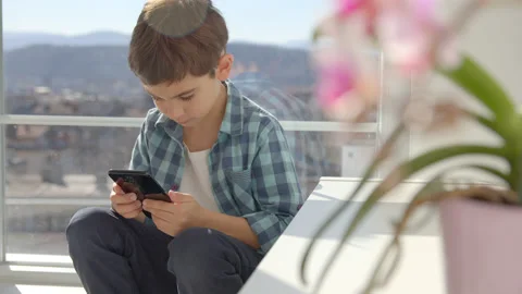 Boy sitting on windowsill, using mobile cell phone, watching video, playing game Stock Footage 171091281